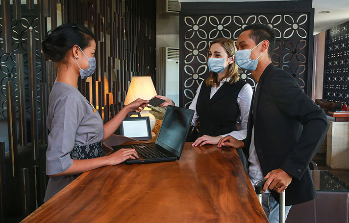 Couple and receptionist at counter in hotel wearing medical masks as precaution against coronavirus